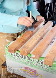 a woman standing next to a box filled with wooden planks on top of a table