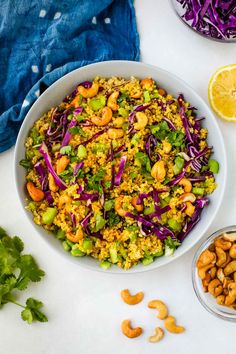 a white bowl filled with colorful salad next to two bowls of nuts and cilantro