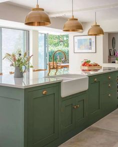 a large kitchen with green cabinets and gold pendant lights over the sink, along with potted plants