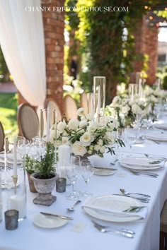 a long table is set with white flowers and silverware for an elegant wedding reception