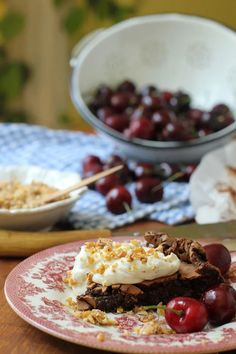 a piece of cake on a plate with cherries and other desserts in the background