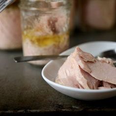 a white bowl filled with sliced meat next to a jar of mustard and a spoon