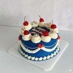 a blue birthday cake with white frosting and cherries