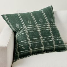 a green and white plaid pillow sitting on top of a white couch next to a wall