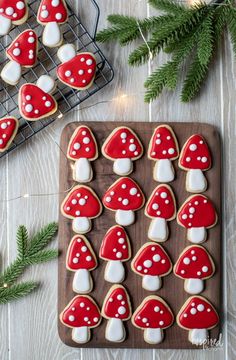 cookies decorated with red and white mushrooms are on a wooden board next to fir branches