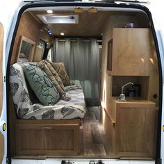 the interior of a camper van with its door open and pillows on the bed