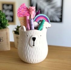 a white bear shaped pen holder with pens, markers and pencils in it on a table