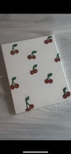 a white canvas with red and green cherries on it, sitting on a table