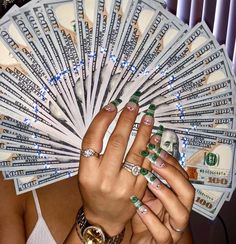 a woman's hands with green and white nail polish holding money