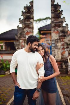 a man and woman standing next to each other in front of an old building with stone pillars