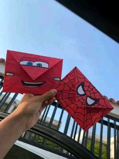 someone is holding up a paper spider man and a red envelope with the face of cars on it