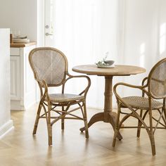 two wicker chairs and a round table in front of a white wall with sunlight streaming through the window