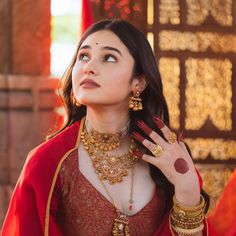 a woman in a red outfit with gold jewelry on her neck and hand near her ear