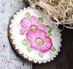 a decorated cookie with pink flowers on it sitting next to some shredded grass and straw