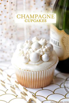 a cupcake with white frosting and marshmallows on top next to a bottle of champagne