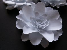 three white paper flowers sitting on top of a black tableclothed surface with one large flower in the center