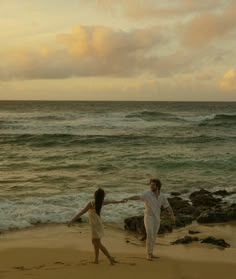 two people are walking on the beach holding hands