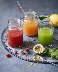 three jars filled with different colored drinks on top of a tray next to lemons