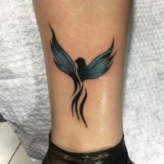 a tattoo on the ankle of a woman's leg with a black bird and blue wings