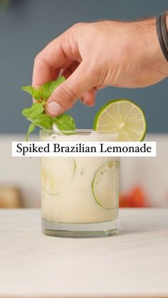 a person is sprinkled with green leaves and limes in a glass filled with lemonade