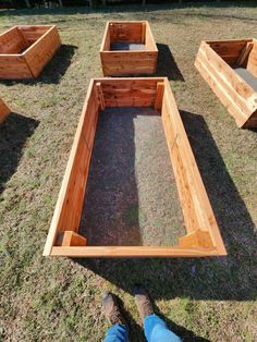 a person standing in front of some wooden raised garden beds with grass and gravel inside