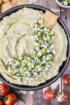 a bowl filled with hummus, cucumber and crackers next to tomatoes