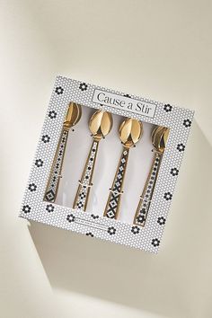 three golden spoons in a white box with black and white designs on the sides