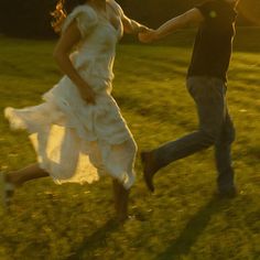 two people running in the grass holding hands