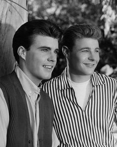 black and white photograph of two young men wearing vests, smiling at the camera