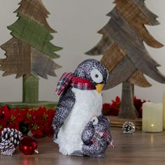 a stuffed penguin sitting on top of a wooden table next to christmas decorations and candles