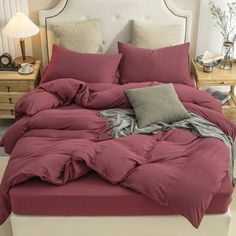 a bed with red sheets and pillows on top of it in a room next to two nightstands