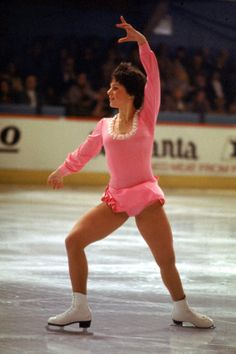 a female figure skating on an ice rink wearing a pink outfit and white socks with her arms in the air