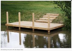 a wooden dock sitting on top of a body of water next to a lush green field