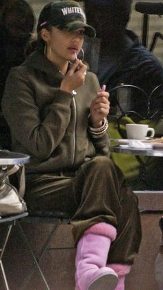 a woman sitting at a table talking on a cell phone while holding a cup in her hand