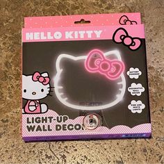 the hello kitty light up wall decoration is in its box on the counter top, it's pink and white