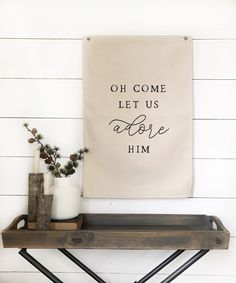 a wall hanging above a shelf with vases on it and a sign that says, oh come let us adore him