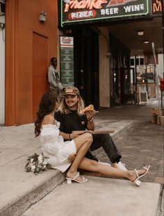 two people sitting on the sidewalk eating pizza