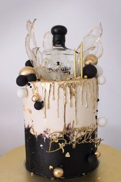 a black and white birthday cake with gold decorations on the top is topped with a bottle of booze