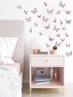 a bedroom with a pink bed, nightstand and wall decals that have purple butterflies on it