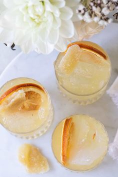 three glasses filled with lemonade sitting on top of a white table next to a flower