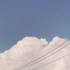 an airplane is flying high in the sky with power lines below and clouds behind it