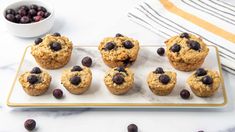 blueberry muffins on a white plate next to a bowl of berries