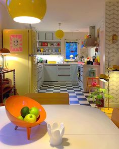 an orange bowl filled with fruit sitting on top of a white table in a kitchen