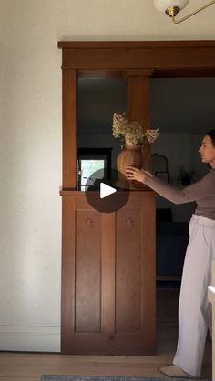 a woman standing in front of a wooden cabinet holding a vase with flowers on it