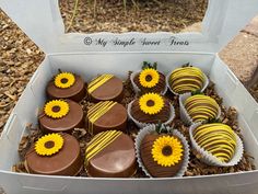 a box filled with chocolate covered sunflowers on top of grass and dirt next to trees