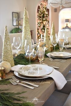 the table is set for christmas dinner with silverware and gold decorations on top of it