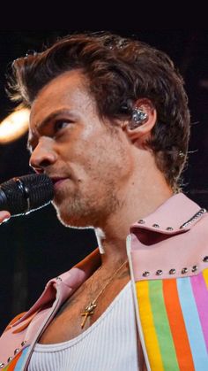 a man in a pink jacket holding a microphone and singing into a mic on stage