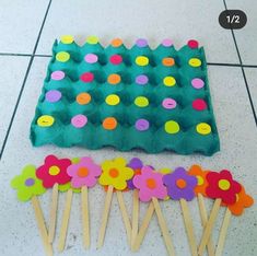 several pops sticks with flowers and dots on them next to an egg carton filled with eggs