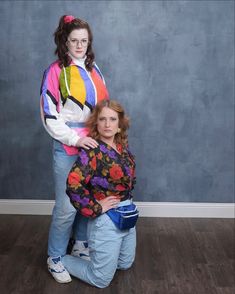 two women standing next to each other in front of a wall