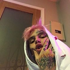 a man with pink hair and piercings on his face is covering his face by a white hoodie